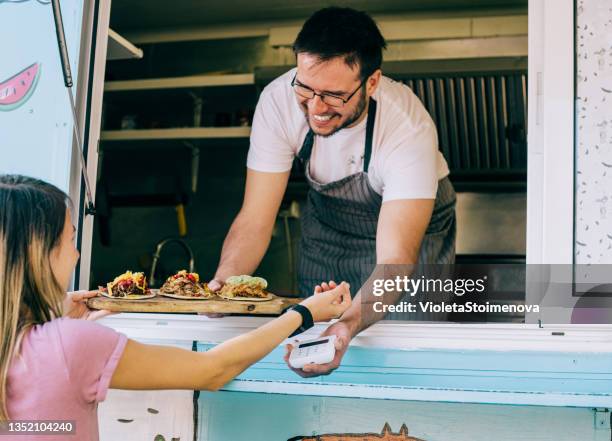 woman buying tacos from food van and using smart watch. - food truck payments stock pictures, royalty-free photos & images