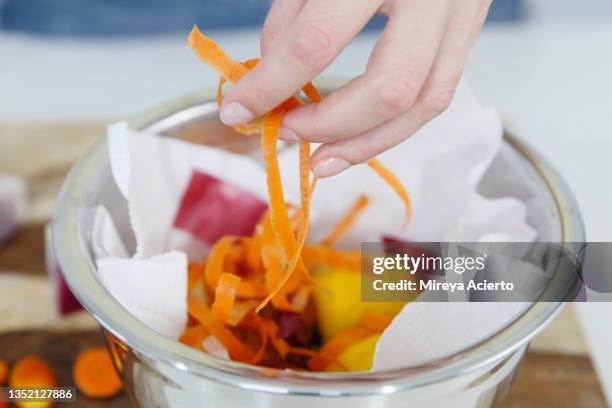 detail of a caucasian woman's hand placing carrot peels into a metal bowl with leftover vegetables in a  brightly lit kitchen. - carrot stock photos et images de collection