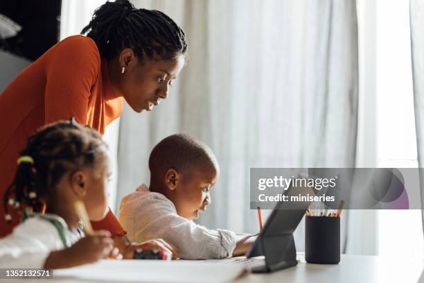 madre seria ayuda a sus hijos a hacer su tarea en una sala de estar - educación en el hogar fotografías e imágenes de stock