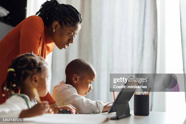 serious mother helps her children to do their homework in a living room - school tablet stockfoto's en -beelden