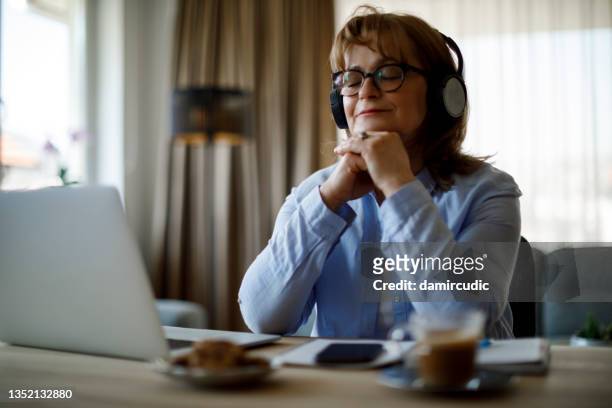 smiling senior woman with wireless headphones enjoying music at home - mindfulness stockfoto's en -beelden