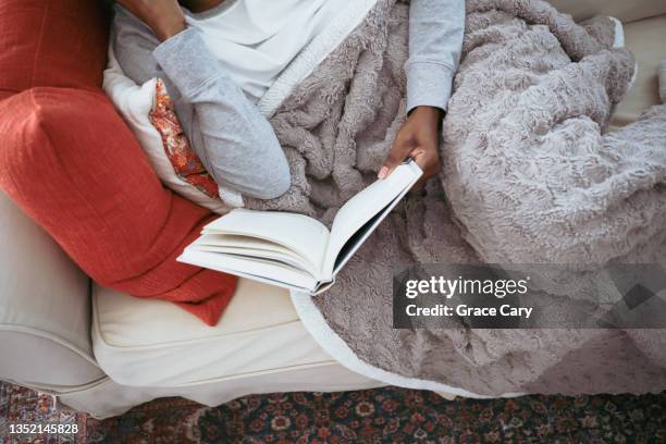 woman reads book on sofa - cobertor imagens e fotografias de stock