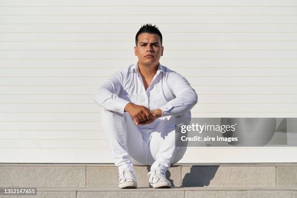 man looking at the camera dressed in white sitting on the step clasping his hands. - white pants stock pictures, royalty-free photos & images