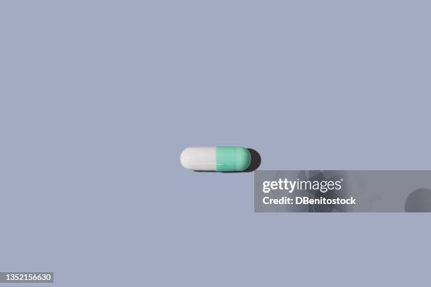 white and green pill with hard shadow on blue-gray background. medicines, drugs, hallucinogens and creativity concept. - antibiotics stock pictures, royalty-free photos & images