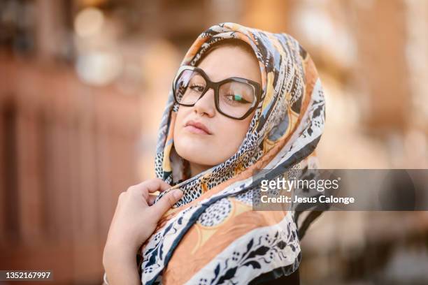 caucasian girl, with fashion glasses and hijab, looking at the camera, with a serious expression. with a street background. girls, muslim, islam, religion, students and business women concept - modern arab woman stockfoto's en -beelden