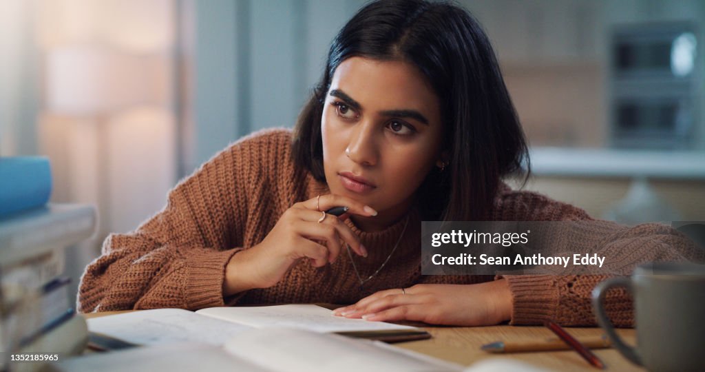 Shot of a young woman looking thoughtful while studying at home