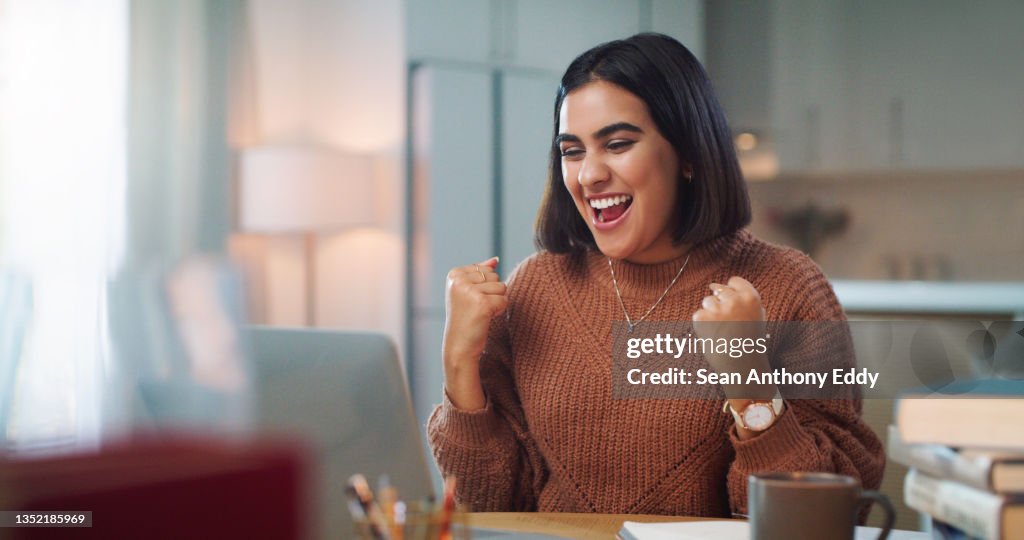 Shot of a young woman cheering while using a laptop to study at home