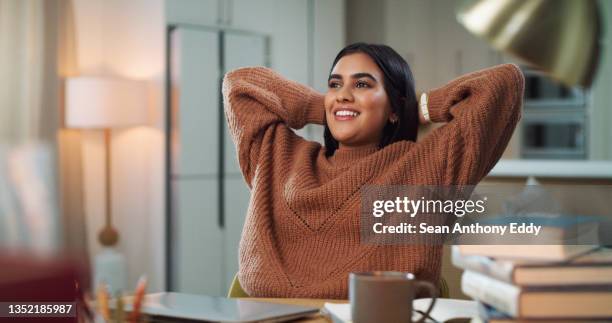 shot of a young woman sitting with her hands behind her head while studying at home - beëindigen stockfoto's en -beelden