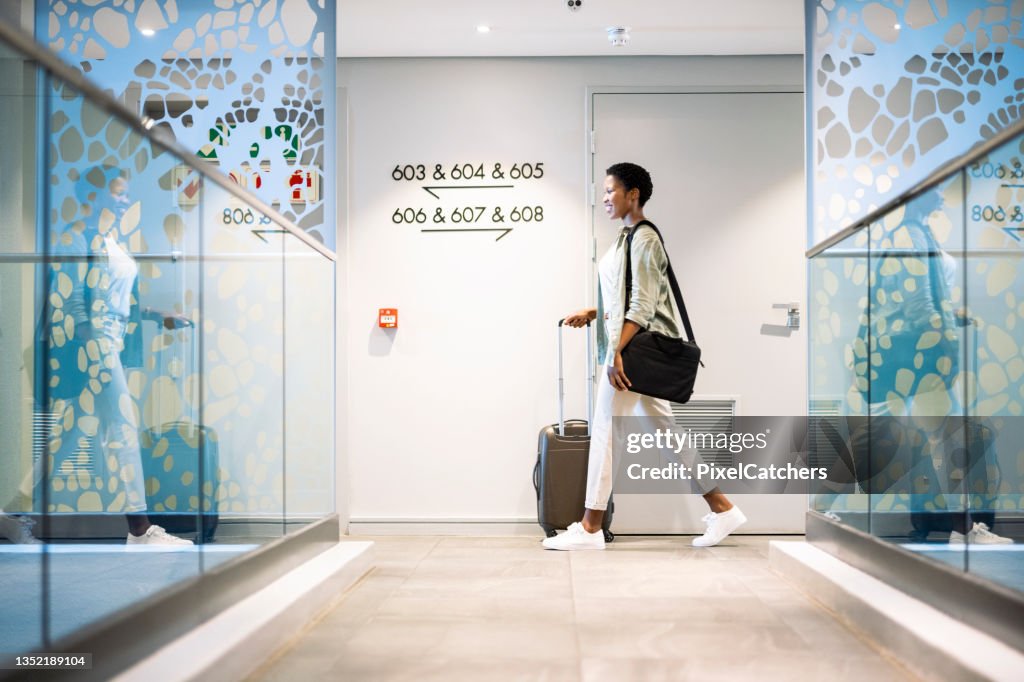 Jeune femme marchant avec des bagages à roues dans le couloir de l’hôtel