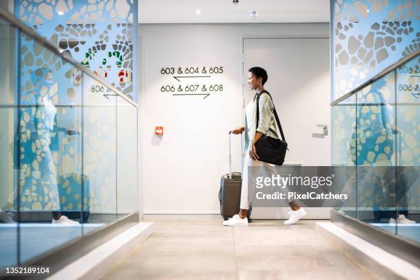 young woman walking with wheeled luggage in hotel corridor - hotel stock pictures, royalty-free photos & images