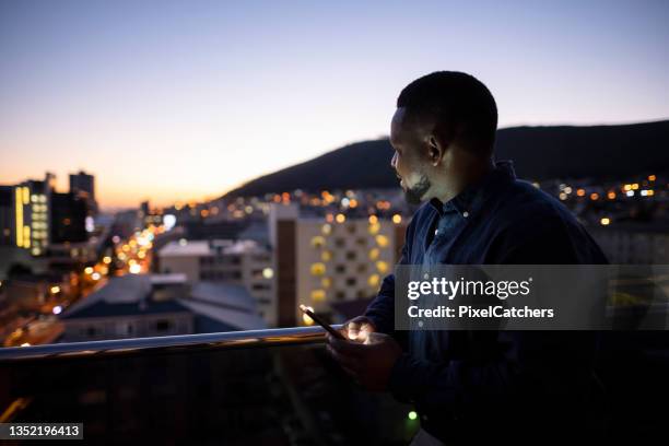 african businessman looking at view of city at dawn holding phone - south africa business stock pictures, royalty-free photos & images