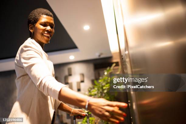 happy african businesswoman pressing elevator button in hotel lobby - lift button stock pictures, royalty-free photos & images