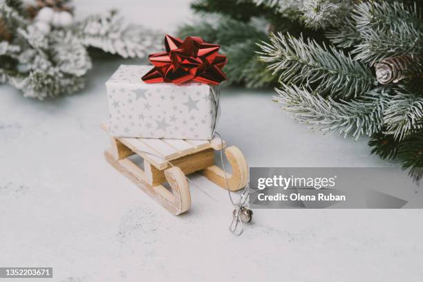 gift box decorated with silver stars and red bow on wooden toy sled - kegelvrucht stockfoto's en -beelden