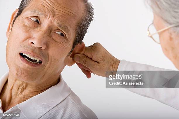 close-up of a senior woman holding a senior man's ear - ear close up women stock-fotos und bilder