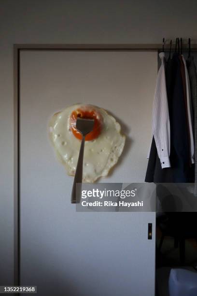 a giant fried egg stuck to the wall with a fork. - invisible man stock-fotos und bilder