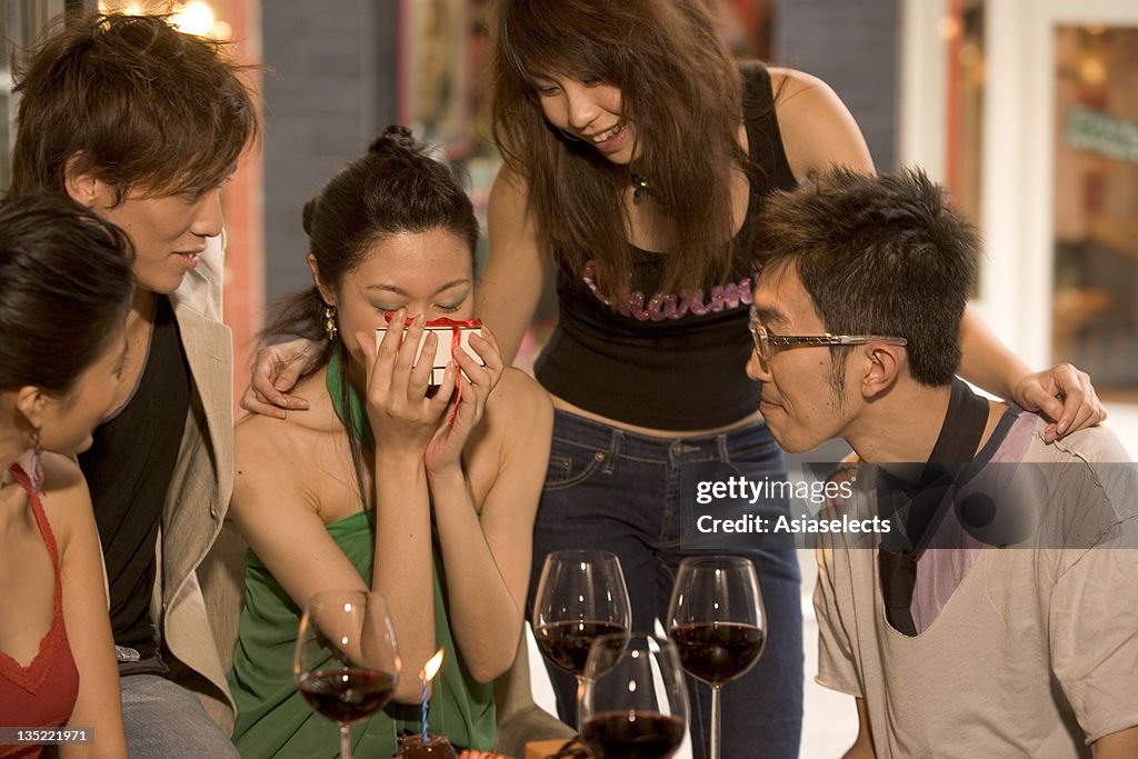 Close-up of a young woman holding a gift with their friends looking at her