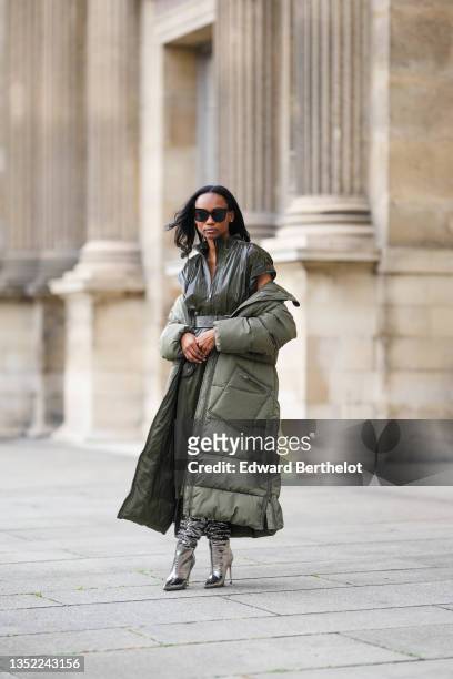 Emilie Joseph @in_fashionwetrust wears black sunglasses, rhinestones earrings, an oversized quilted recycled shell long puffer jacket from Ganni, a...