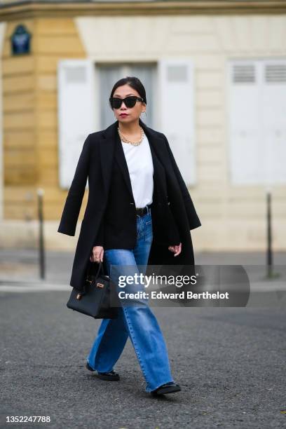 May Berthelot wears black sunglasses, gold earrings, a gold large chain and pearls necklace from Leo Sedim, a white t-shirt, a black wool blazer...