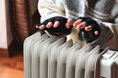 Person heating their hands at home over a domestic portable radiator in winter