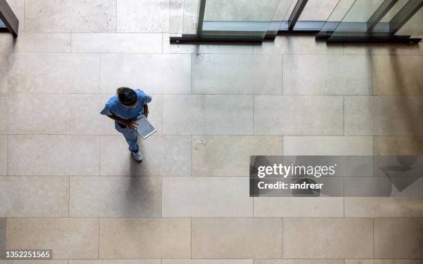 enfermera latinoamericana caminando por el hall de entrada de un hospital mientras mira los resultados de algunas pruebas en una tableta - nhs fotografías e imágenes de stock