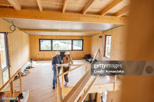 arquitecta e ingeniera civil analizando plano en casa de madera incompleta - foundations conversations with suits fotografías e imágenes de stock