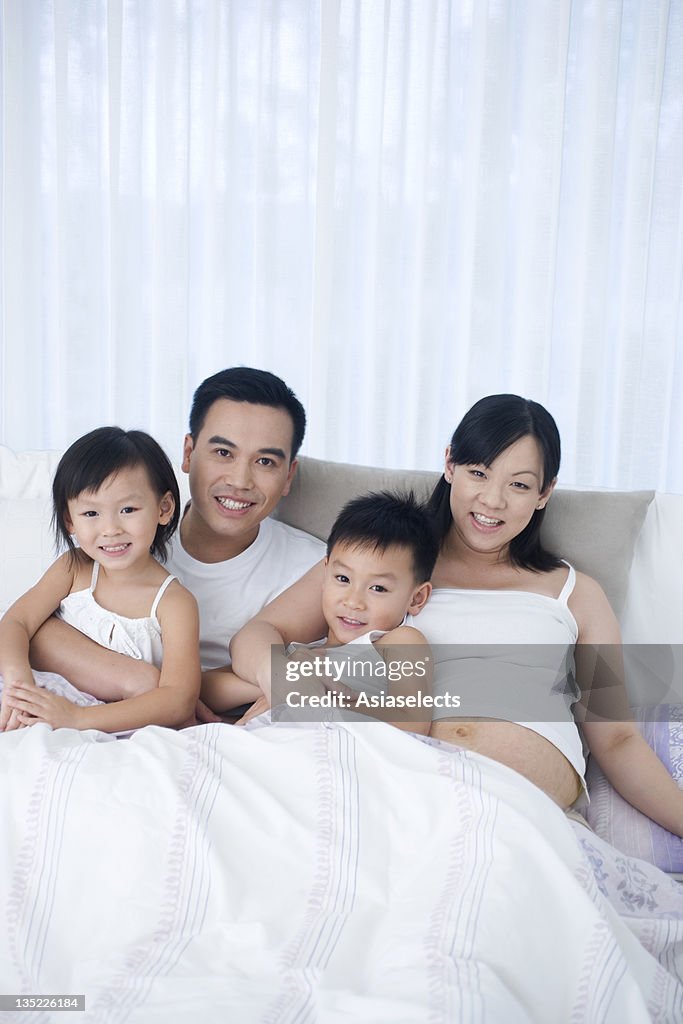 Portrait of parents sitting with their son and daughter on the bed smiling