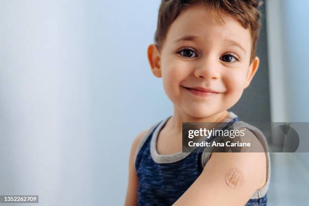 ワクチンを受けた後、包帯を巻いた腕を見せる少年 - vaccination ストックフォトと画像