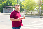 An adult man prone to fatness with two glasses of ice cream on a sunny day on a city street