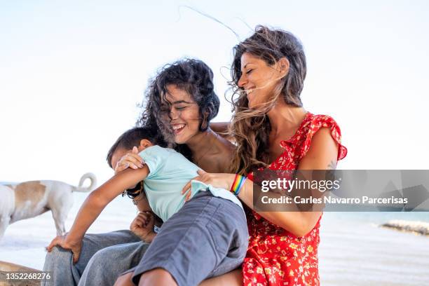 lesbian couple with a rainbow bracelet playing with a kid while sitting outdoors - funny lesbian 個照片及圖片檔