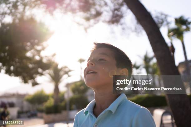 child illuminated by sunshine with happy expression in a city park - face happy sun stockfoto's en -beelden