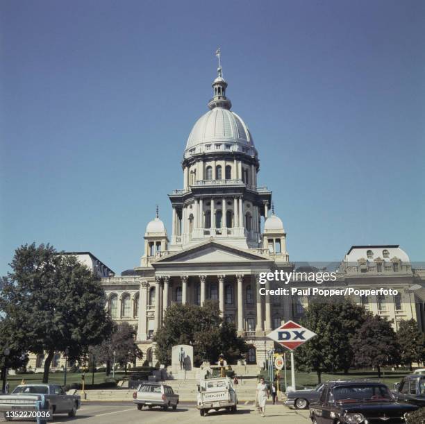 Cars and pick up trucks parked in front of the Illinois State Capitol building in the City of Springfield in Illinois, United States in October 1965.