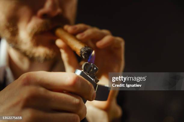 a close up of a man lighting a cigar on a black background, only a half of his face is in the frame - cereal bar stockfoto's en -beelden