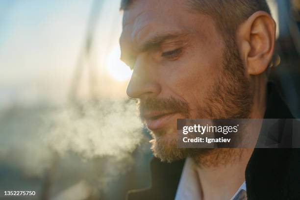 close -up of a serious man smoking man looking down, standing on a roof during the dawn - quitting smoking stock pictures, royalty-free photos & images