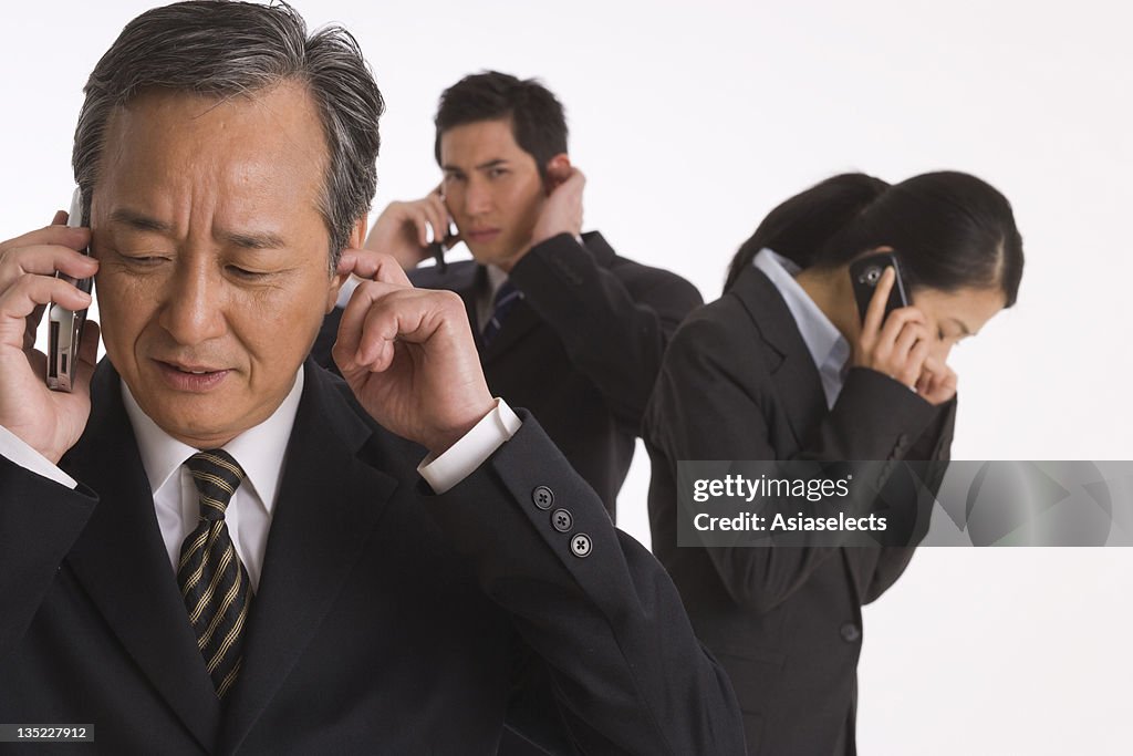 Three business executives standing and talking on mobile phones