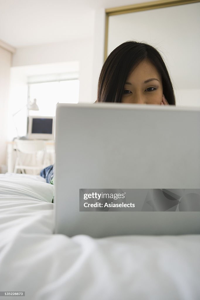 Young woman lying on the bed and using a laptop