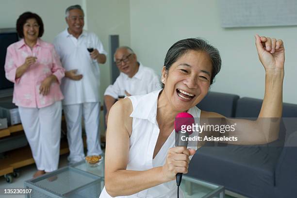 close-up of a senior woman singing into microphone with her friends in the background - senior man dancing on table stock-fotos und bilder
