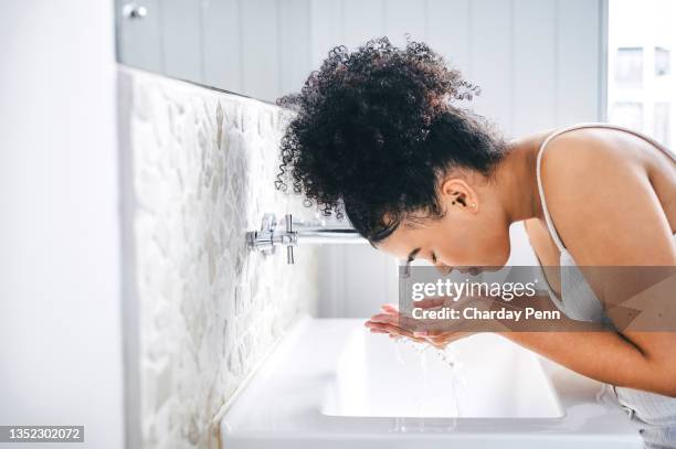 aufnahme einer jungen frau, die ihr gesicht in ihrem waschbecken wäscht - gesichtsreinigung stock-fotos und bilder