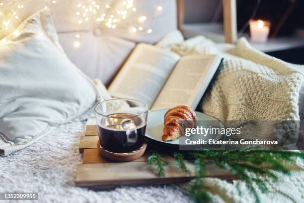 a croissant and a cup of coffee on a wooden tray in a cozy atmosphere. - winter and warm glow stock-fotos und bilder