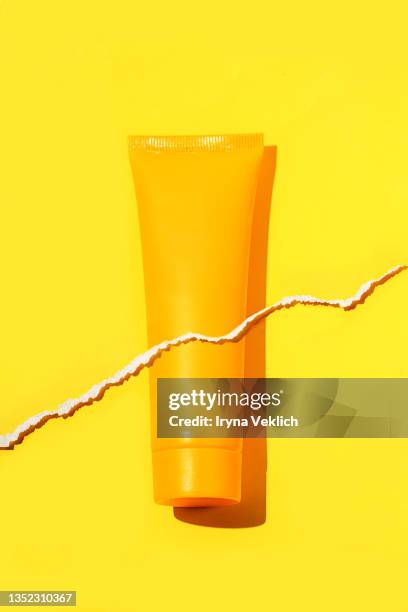 orange tube of organic  moisturizing facial cream  or hand cream, suntan lotion on yellow color background with torn paper effect. routine step for healthy skin care. - creme tube ストックフォトと画像