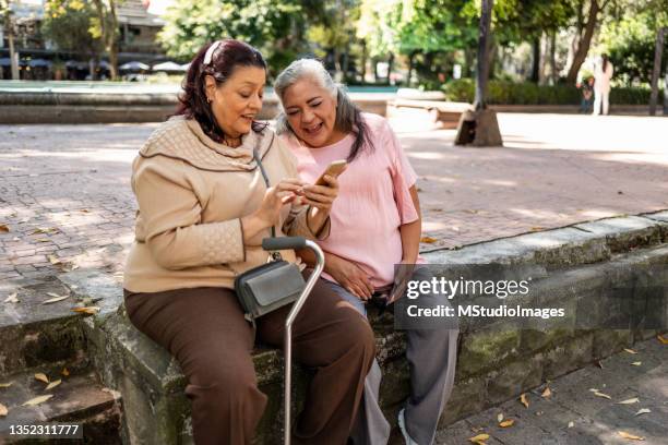 two senior hispanic women using mobile phone - walking cane stock pictures, royalty-free photos & images
