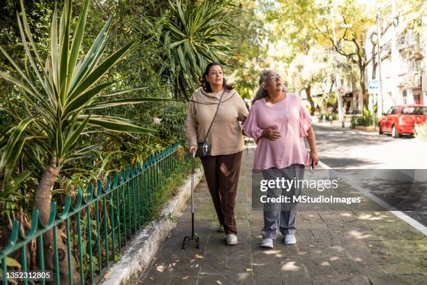 two senior women walking around the park - stick stock pictures, royalty-free photos & images