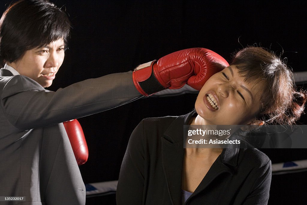 Businesswomen being hit by her opponent in a boxing ring