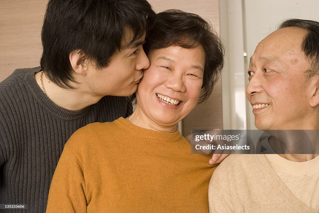Close-up of a young man kissing his mother with a senior man looking at them