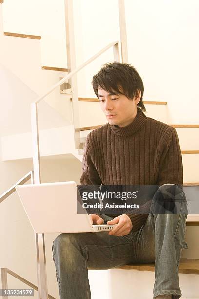 mid adult man sitting on a staircase and using a laptop - high collar ストックフォトと画像
