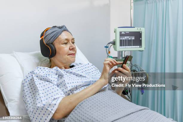 ältere frau mit krebs mit smartphone während des krankenhausaufenthalts - cellphone cancer illness stock-fotos und bilder