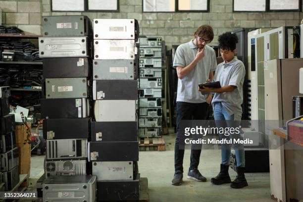 male and female coworkers discussing over clipboard while standing in computer recycling plant - computer part bildbanksfoton och bilder