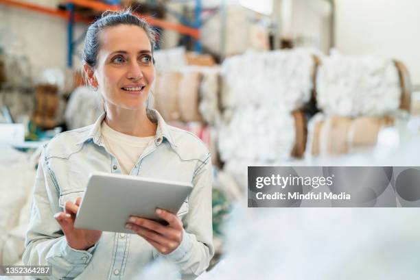 female worker standing inside recycling centre while typing on digital device during daytime - e waste stock pictures, royalty-free photos & images