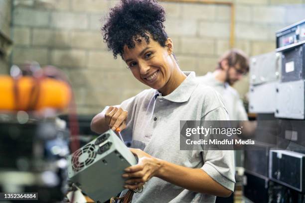 african american female warehouse worker looking at the camera while disarming computer component in recycling plant - repairing electronics stock pictures, royalty-free photos & images