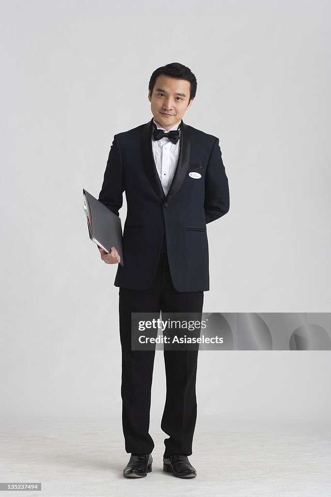 Portrait of a waiter holding a menu and standing with hands behind back