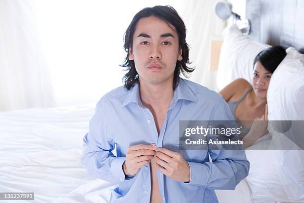 portrait of a young man buttoning his shirt - buttoning shirt stockfoto's en -beelden